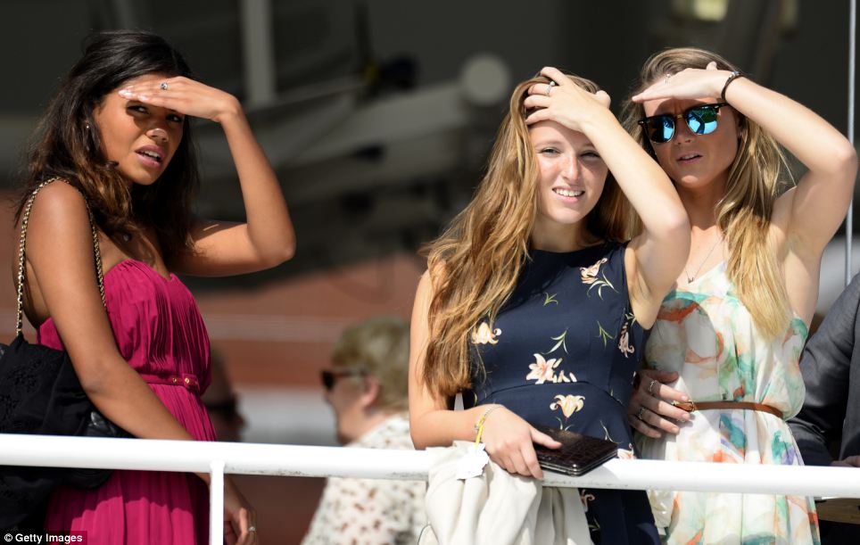 Feeling the heat: Three spectators shield their eyes from the sun as they watch today's runners walk around the paddock ahead of the day's racing